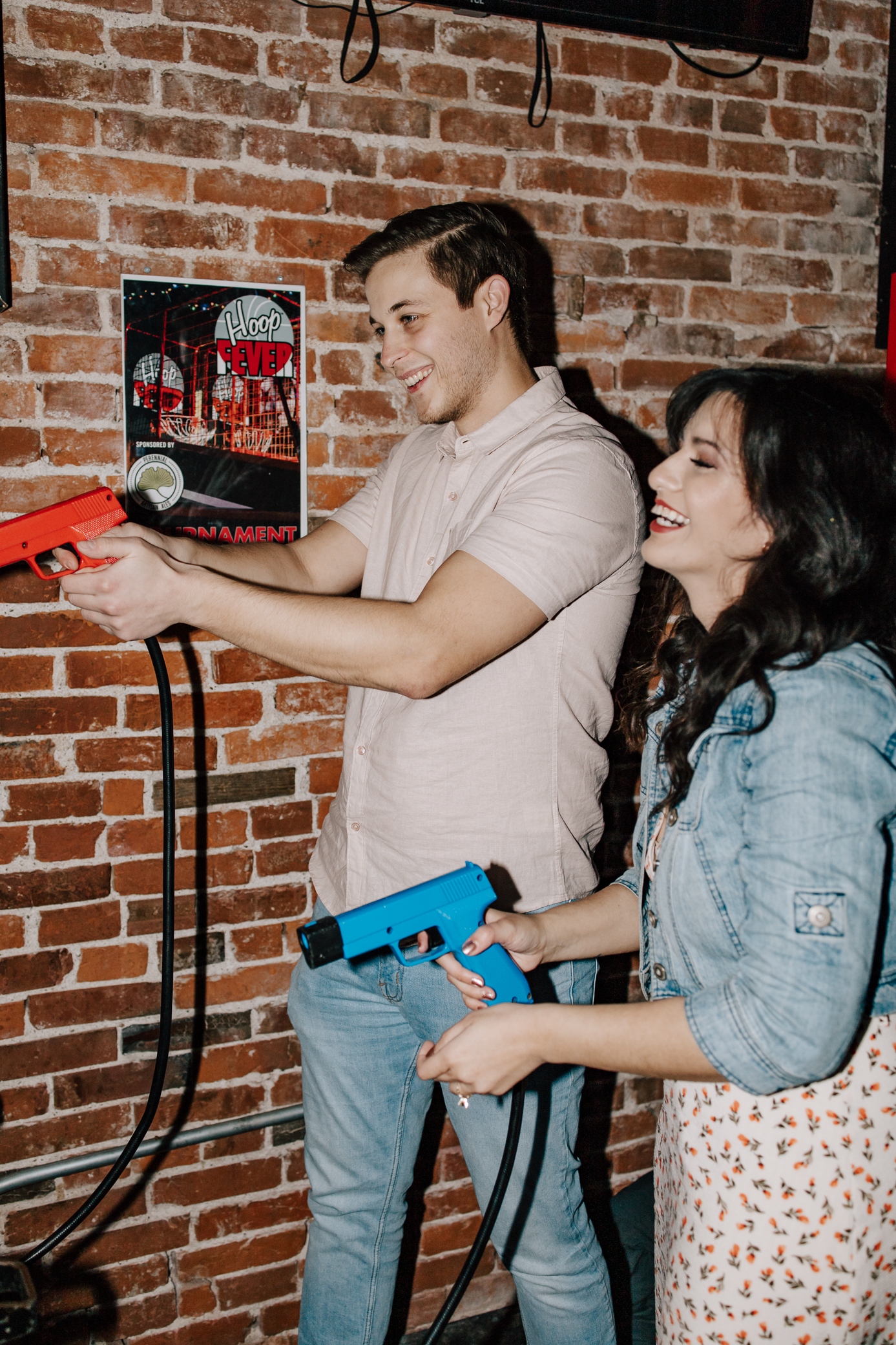 A couple laughs while holding toy guns while playing an arcade game.