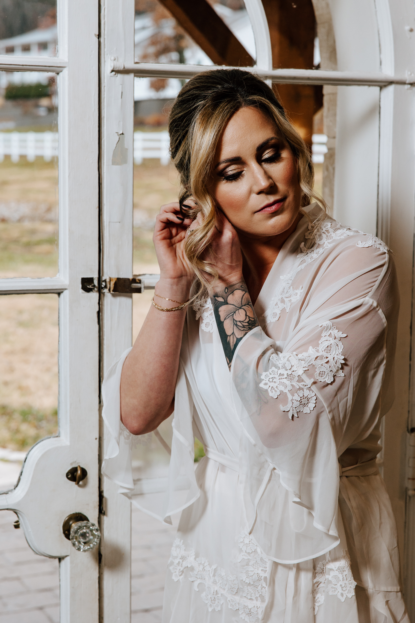 A tattooed bride wears a white robe while she puts her earrings on in the doorway of the bridal suite at Knotting Hills in Pevely, Missouri.