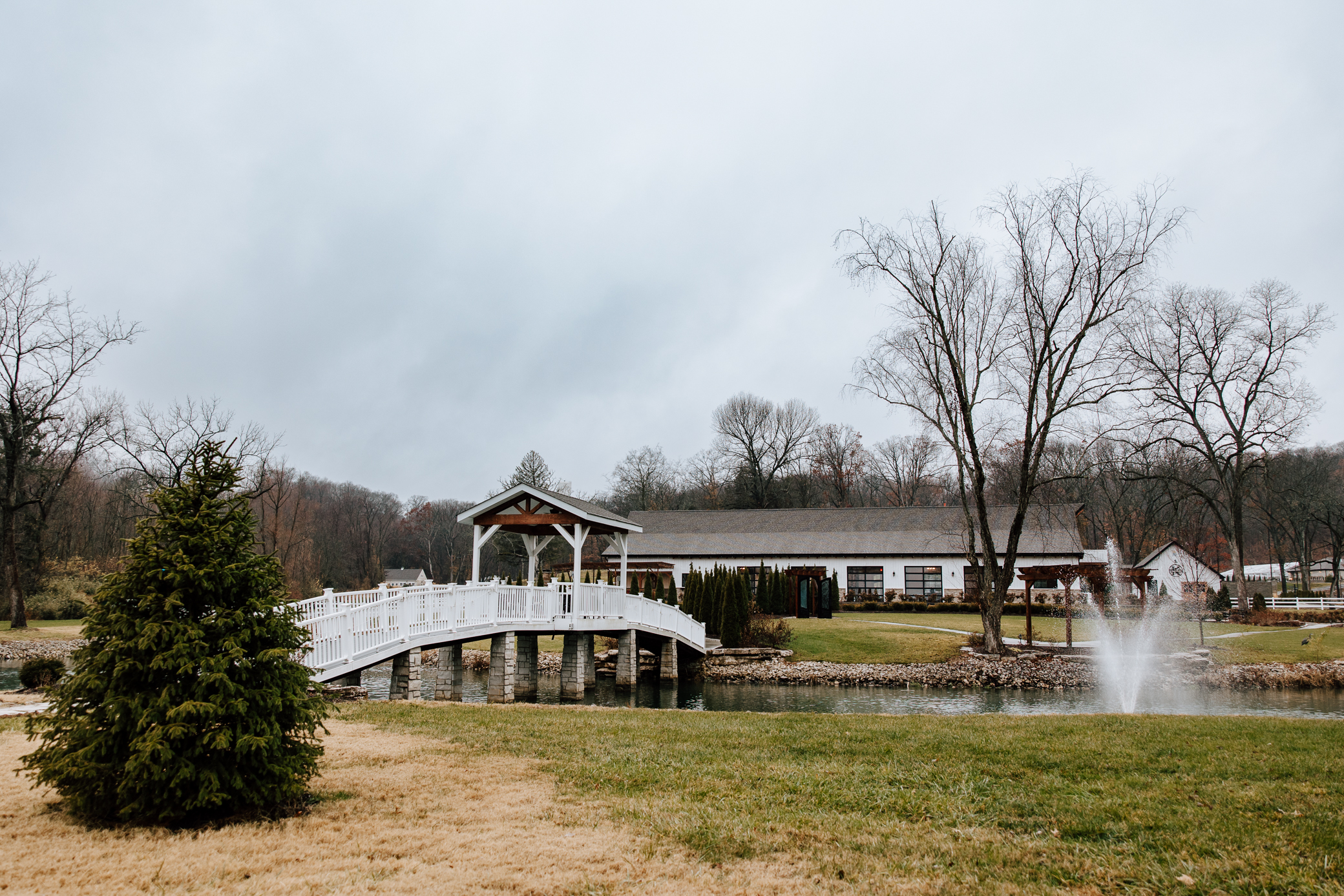 A view of the main venue at Knotting Hills in Pevely, Missouri as seen from the bridal suite. A white wooden bridge is seen directly over the water which connects the bridal suite to the ceremony space and reception hall.