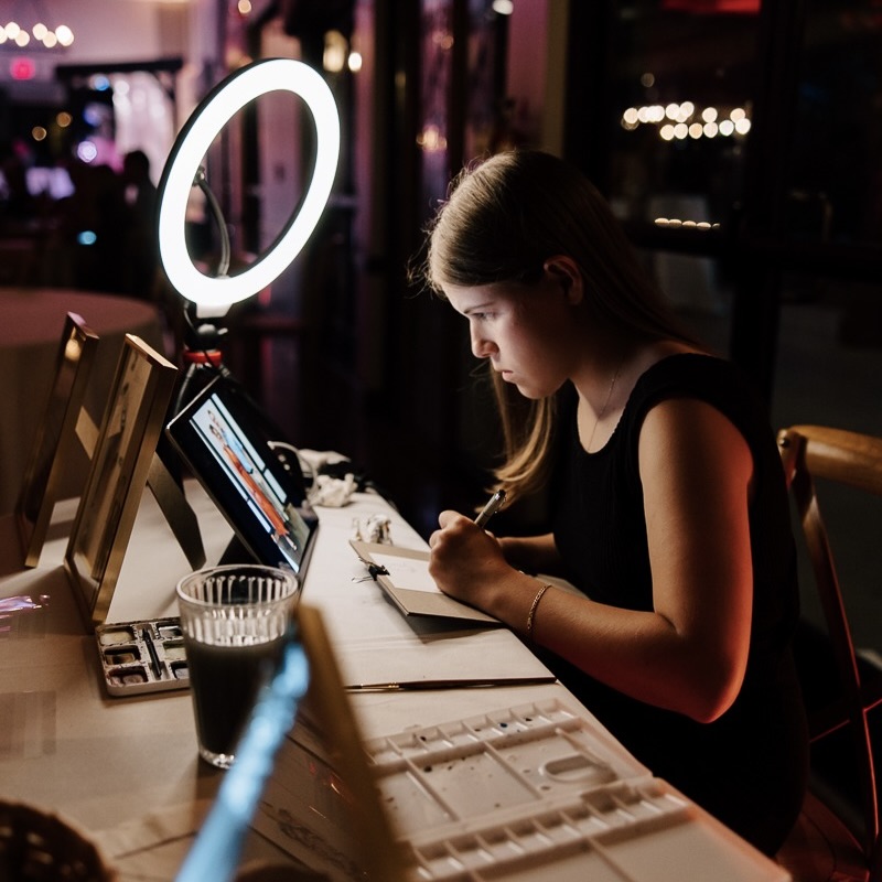 A hired artist sketches a guest portrait at a wedding before painting in watercolor as a guest favor.